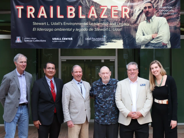 Bradley Udall, Jonathan Nez, Tom Udall, Burr Udall, Steve Hussman, and Tess Udall pose under the 'Trailblazer' exhibit banner at U of A Library Special Collections