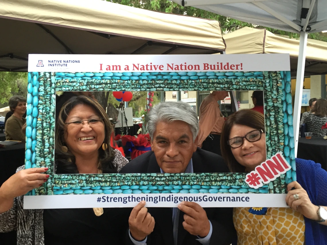 Joan Timeche, Regis Pecos and a third person pose in a papr frame reading "I am a Native Nation Builder"