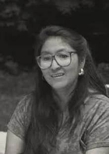 A black and white portrait of Joan Timeche wearing glasses in her 20s